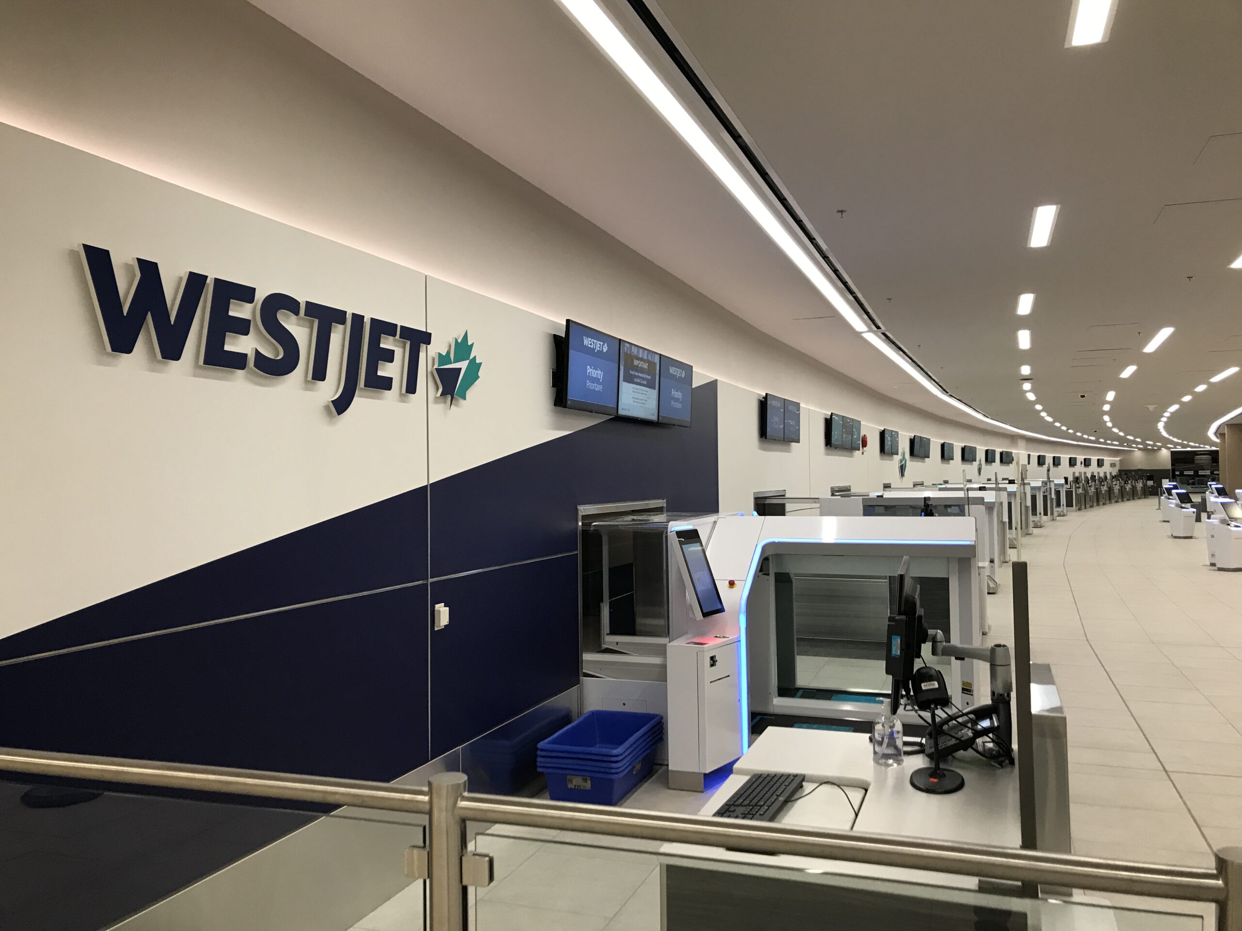 Une rangée de bornes d'enregistrement en libre-service et de comptoirs WestJet dans un terminal d'aéroport vide, avec des écrans suspendus affichant des informations sur les vols.