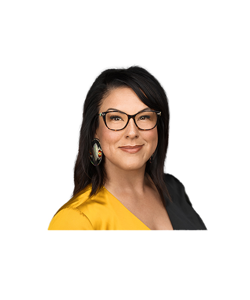 A woman with dark hair and glasses smiles at the camera. She is wearing a yellow and black top and beaded earrings on a plain white background.