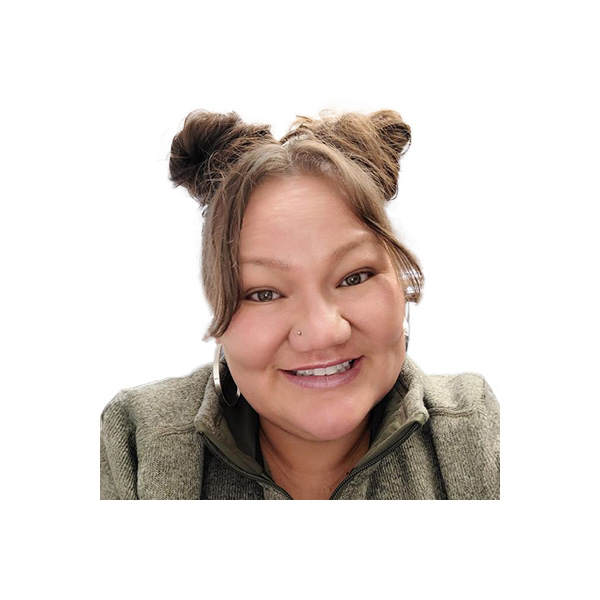 A woman with long brown hair, hoop earrings, and bold eyebrows smiles at the camera. She has a bright complexion and is photographed against a light background.