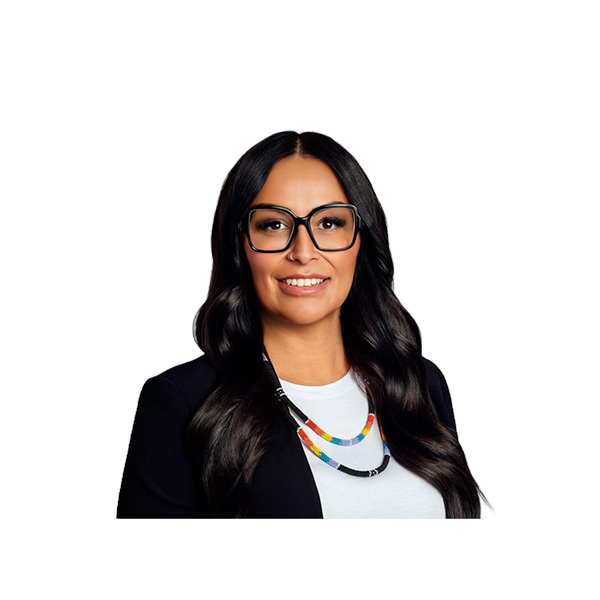 Woman with long dark hair, wearing glasses, a white shirt, a black blazer, and a colorful beaded necklace, smiles at the camera against a plain white background.