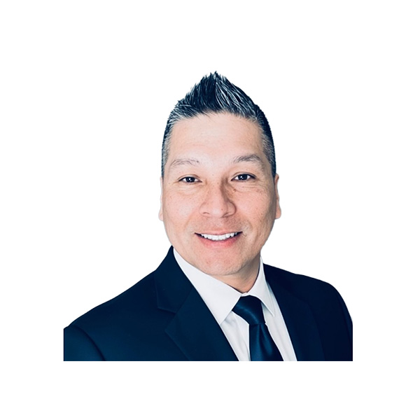 Smiling man with short spiked hair wearing a dark suit, white shirt, and dark tie, posing against a plain white background.